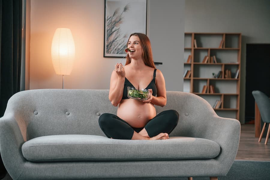 mulher grávida sentada no sofá comendo salada