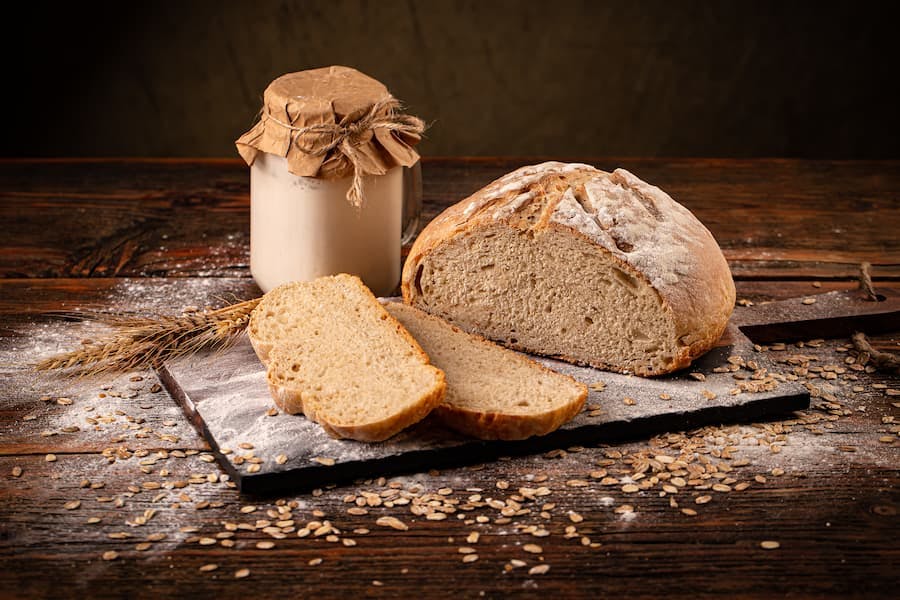 pão caseiro ao lado de pote de vidro com fermento natural levain