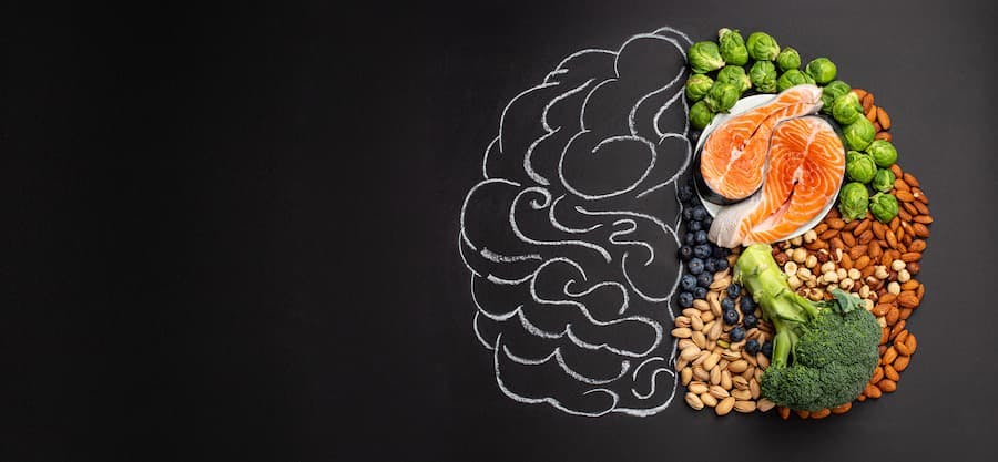Desnho de um cérebro feito num quadro negro com giz, metade dele é ocupado por alimentos saudáveis, peixes, verduras e grãos