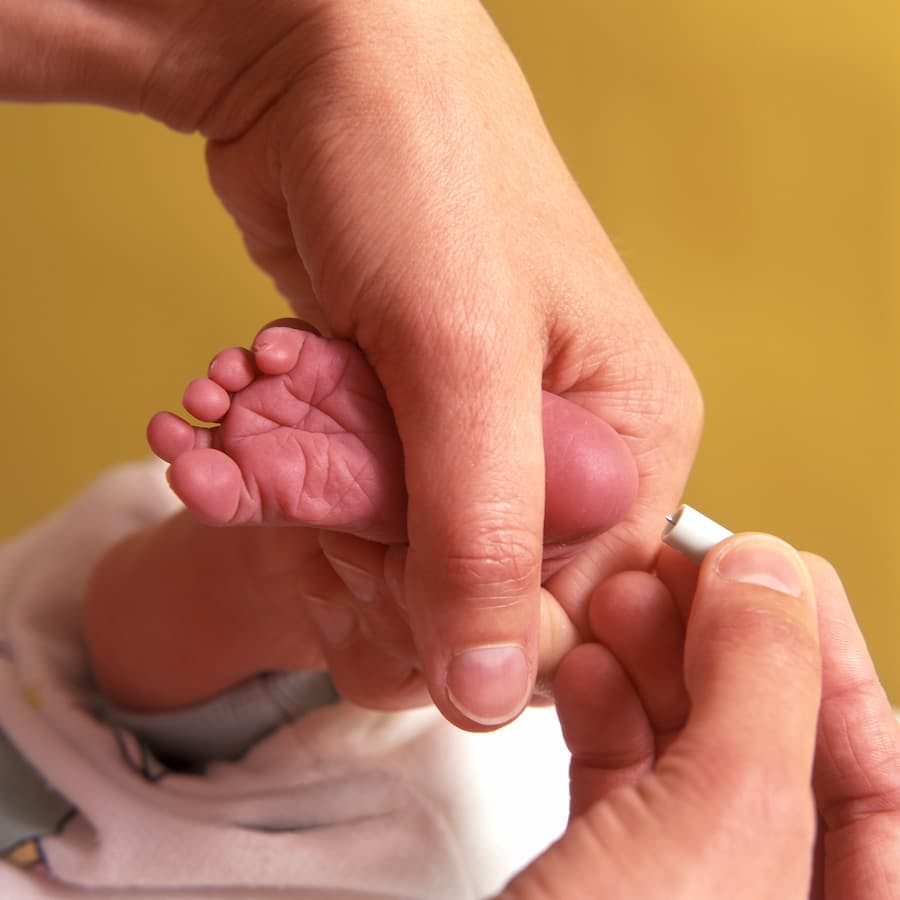 Mãos de adulto colhe sangue de pé de bebê