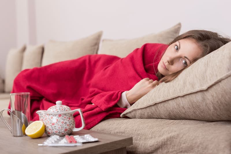 Mulher deitada no sofá com sintomas de gripe, resfriado ou dengue