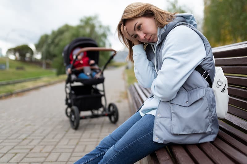 Mulher triste sentada no parque com carrinho de bebê